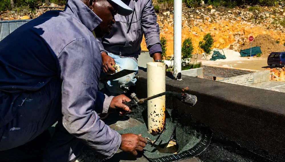 CBM team applying torch-on waterproofing around a drainage outlet on a flat roof in Tokai